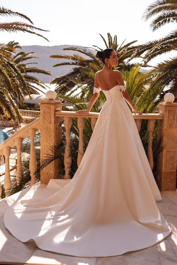 Eine elegant gekleidete Frau im weißen Brautkleid steht auf einer Terrasse mit Palmen