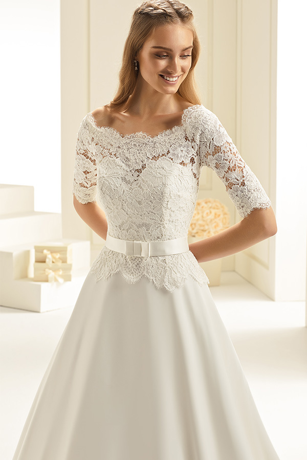 Eine junge Frau lächelt freundlich in einem eleganten weißen Spitzenkleid mit Gürtel