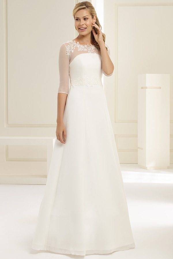 Eine lächelnde Frau in einem eleganten weißen Brautkleid mit Spitzenärmeln