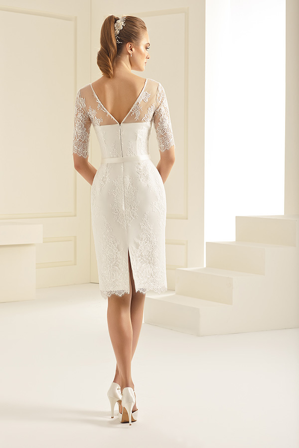 Junge Frau mit blondem Haar trägt ein kurzes weißes Spitzenkleid - Rückansicht