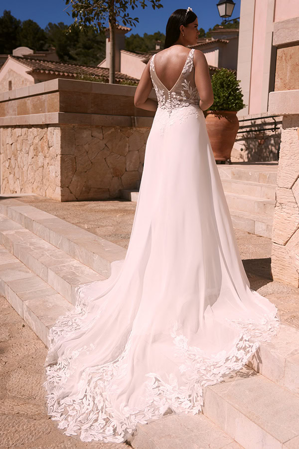 Eine Frau in einem eleganten weißen Brautkleid mit langer Schleppe steht auf Steintreppen