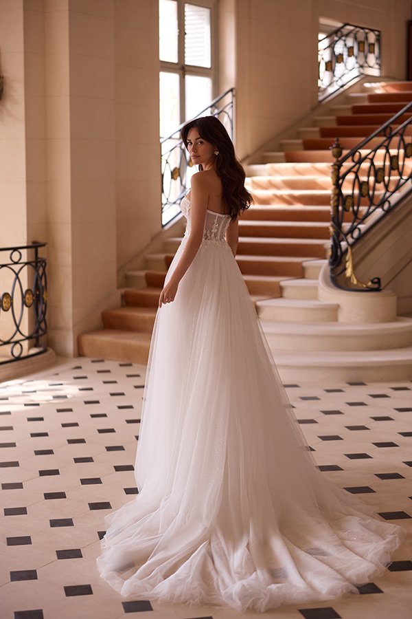 Eine junge Frau im eleganten weißen Brautkleid steht lächelnd vor einer Treppe