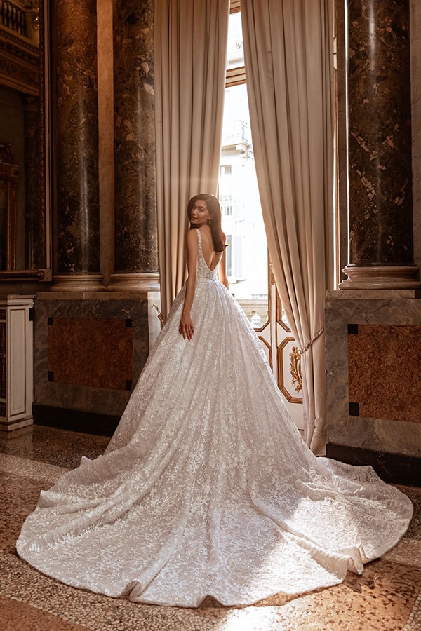 Eine Frau im funkelnden weißen Brautkleid steht anmutig vor einem offenen Fenster