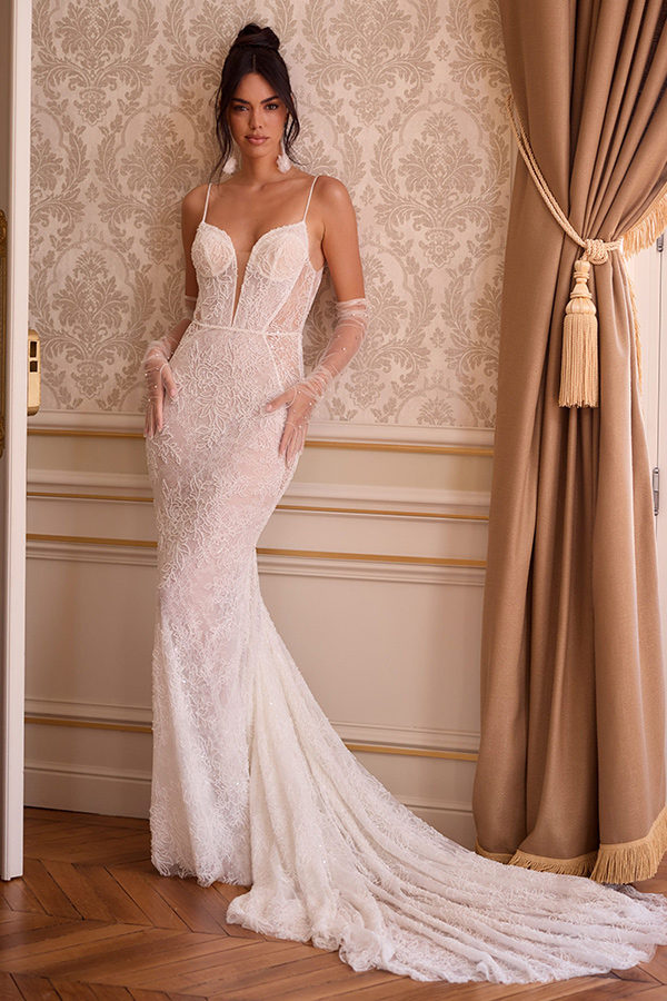 Eine junge Frau mit sinnlichem Blick trägt ein elegantes weißes Spitzenbrautkleid mit Schleppe