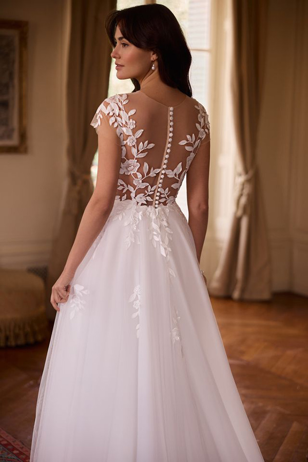 Eine brünette Frau mit elegantem Lächeln trägt ein weißes Kleid mit Spitzenrücken