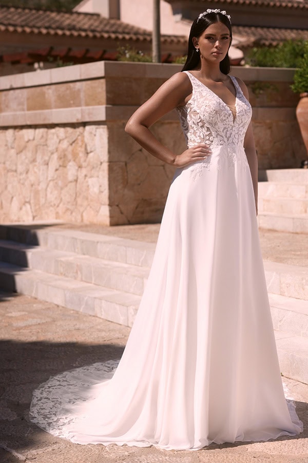 Eine brünette Frau mit ernstem Blick trägt ein elegantes weißes Brautkleid mit Spitze