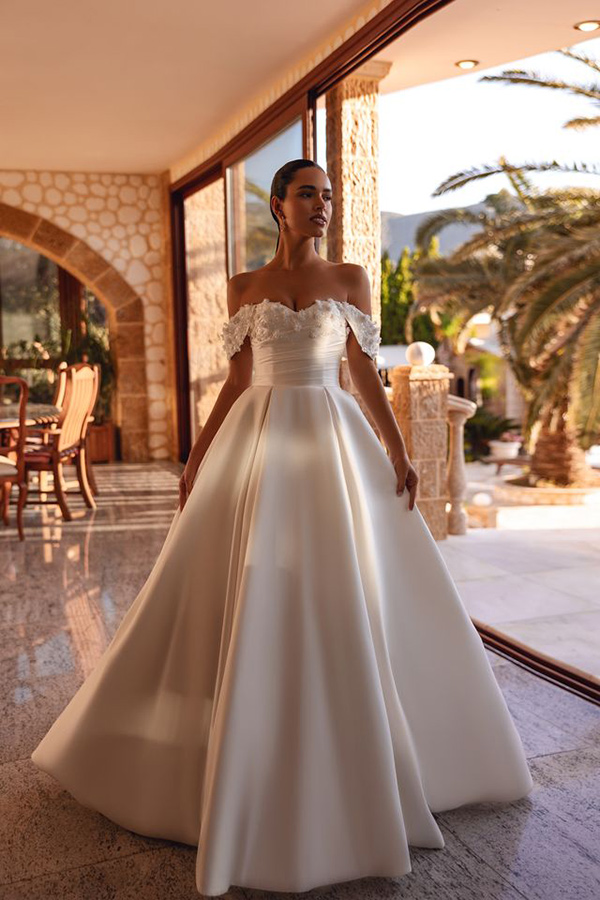 Junge Frau mit elegantem weißem Brautkleid steht ernst im sonnigen Raum