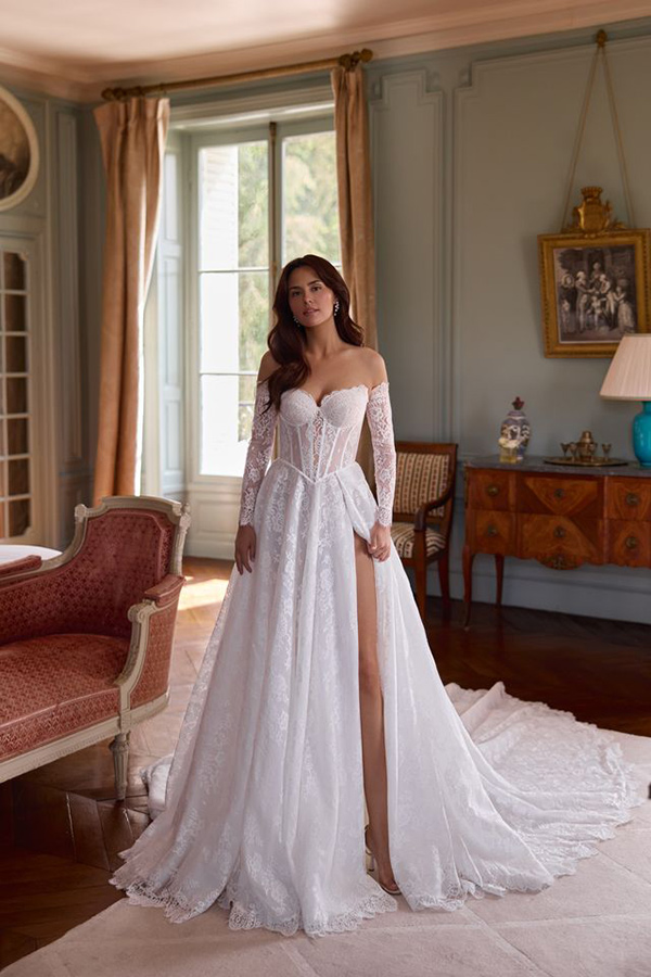 Eine dunkelhaarige Frau lächelt sanft in einem eleganten weißen Brautkleid mit Spitzenärmeln