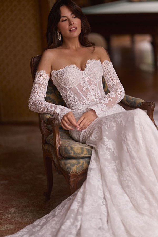 Eine Frau mit langen dunklen Haaren trägt ein elegantes Spitzenbrautkleid und sieht entspannt aus