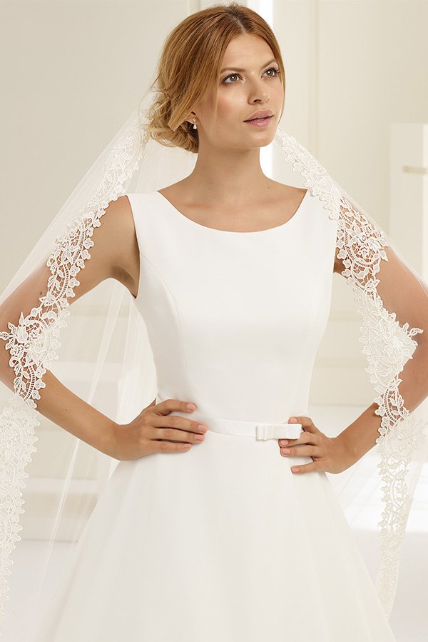 Junge Frau mit sanftem Lächeln trägt elegantes weißes Brautkleid und Spitzen-Schleier