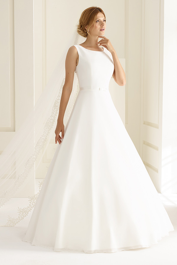 Eine Frau mit blondem Haar trägt ein elegantes weißes Brautkleid und Schleier