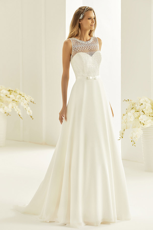 Eine lächelnde Frau im weißen Brautkleid mit durchsichtigem Oberteil und glattem Rock