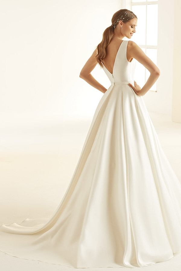 Eine lächelnde Frau im eleganten weißen Brautkleid mit freiem Rücken und Haarschmuck