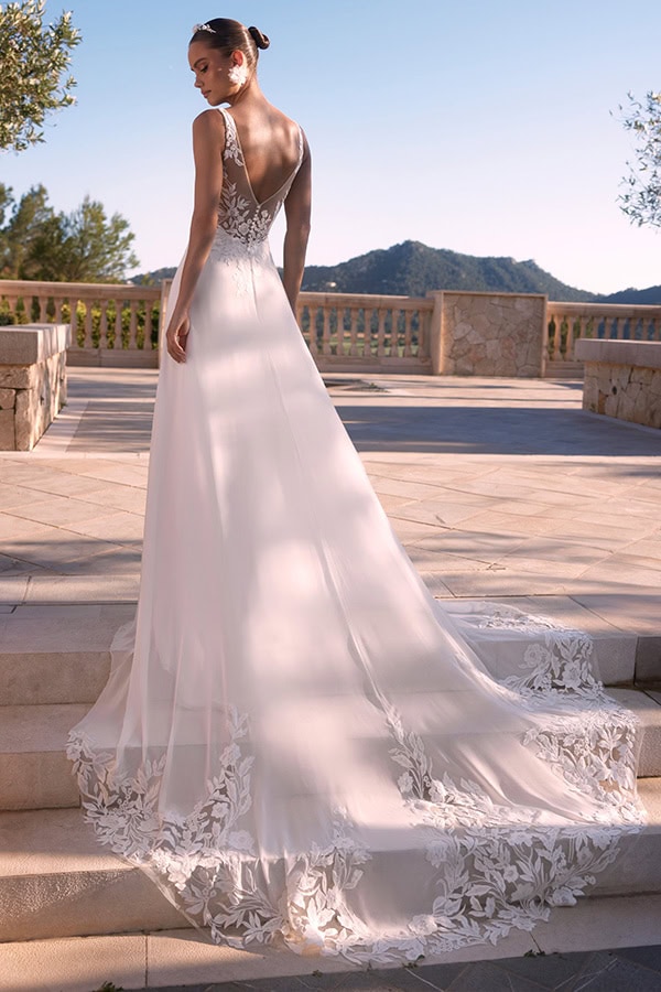 Eine Frau trägt ein elegantes weißes Brautkleid mit floralen Spitzen am Saum