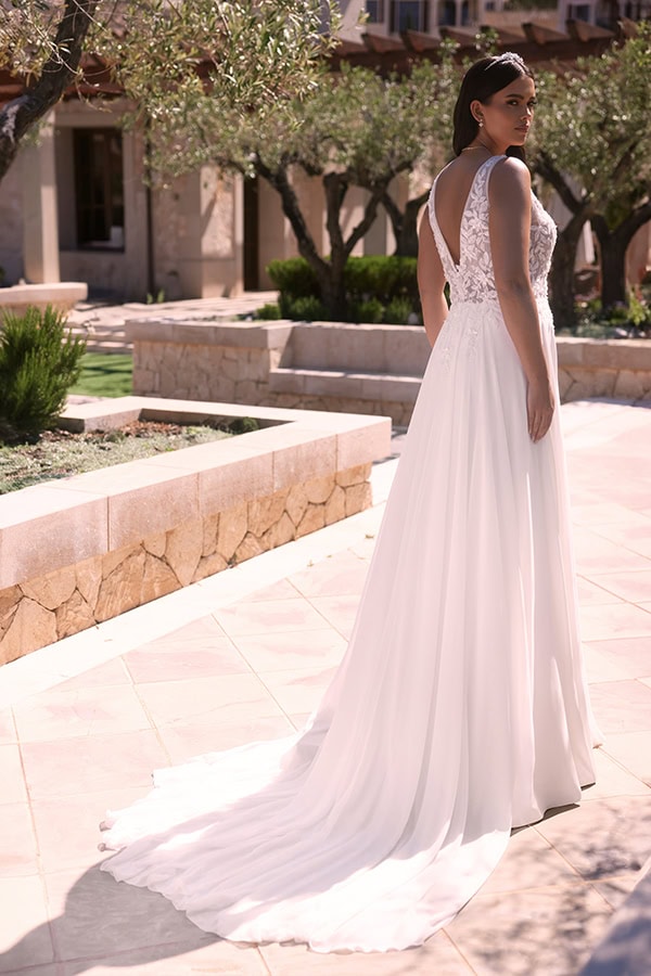 Frau im weißen Brautkleid mit aufwendigem Rücken blickt ernst über die Schulter