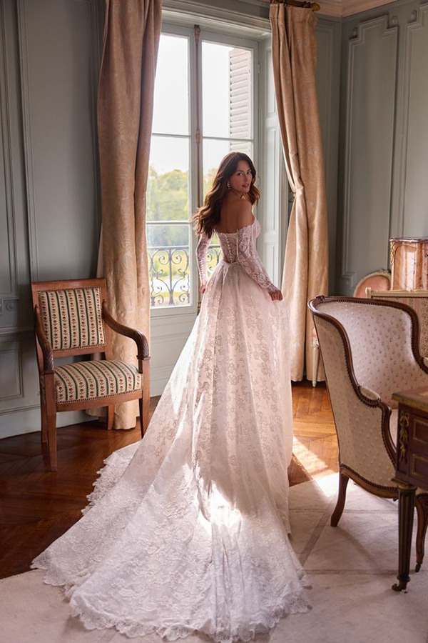 Eine junge Frau mit langen braunen Haaren trägt ein elegantes Spitzenkleid in Weiß