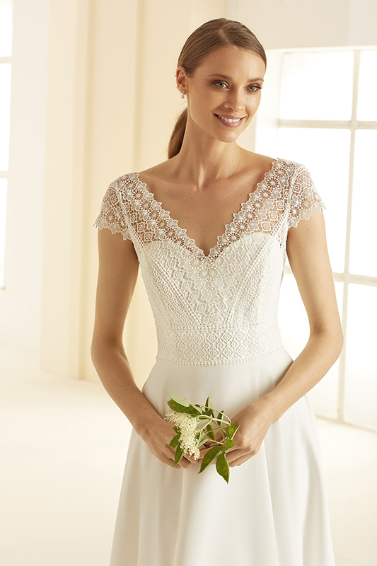 Junge Frau mit freundlichem Lächeln im weißen Spitzenkleid hält grüne Zweige