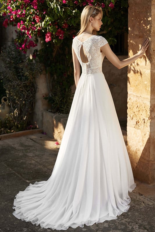 Eine blonde Frau im eleganten weißen Brautkleid steht nachdenklich im Sonnenschein