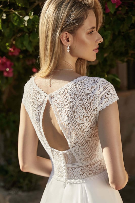 Eine blonde Frau schaut seitlich und trägt ein elegantes, spitzenbesetztes Brautkleid