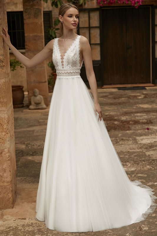 Junge Frau mit sanftem Lächeln trägt ein elegantes weißes Brautkleid im Hof