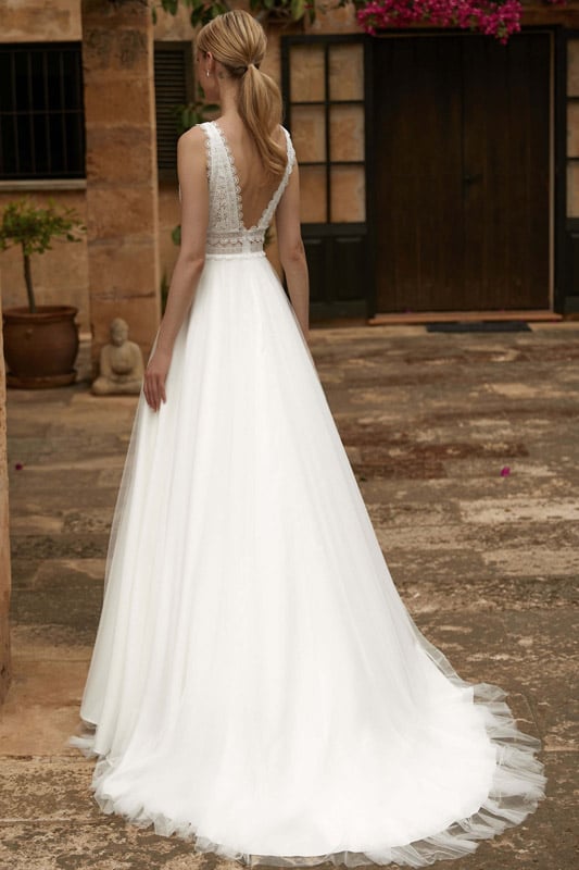 Eine Frau mit blondem Zopf trägt ein elegantes weißes Brautkleid mit Spitze