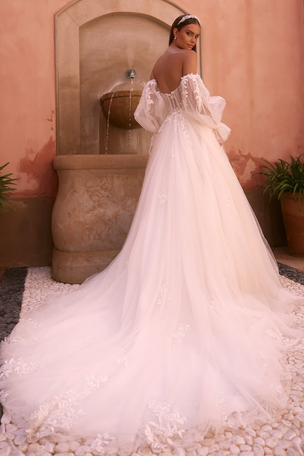 Eine Frau im eleganten weissen Brautkleid mit langen Tüllärmeln schaut lächelnd zurück