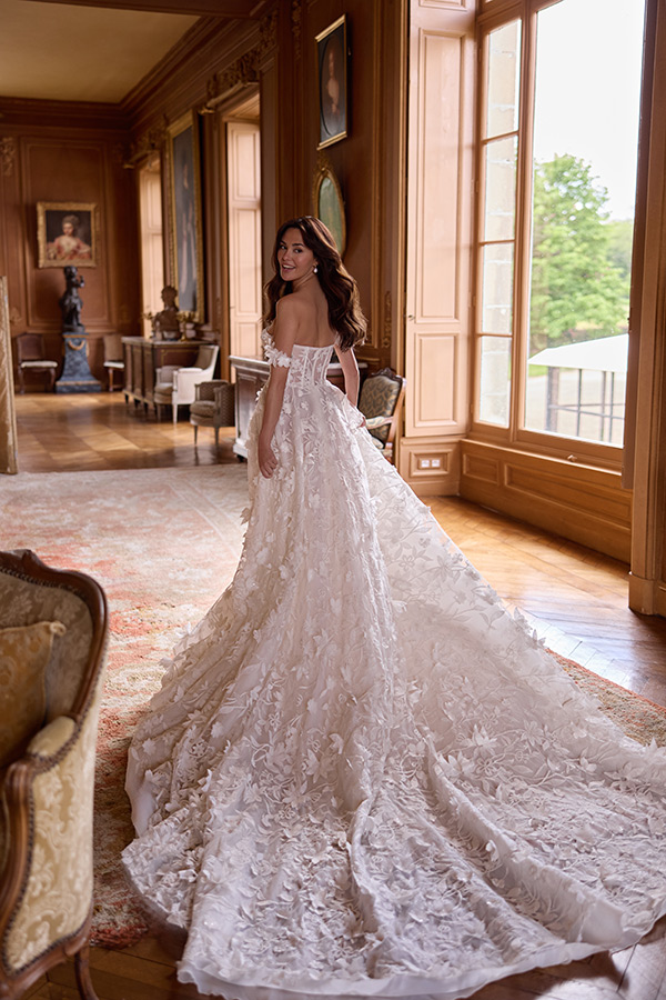 Eine lächelnde Frau in einem weißen, langen Brautkleid mit floralen Details
