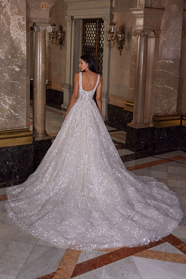 Eine elegante Frau im weißen Brautkleid mit langer Schleppe steht in prunkvollem Saal