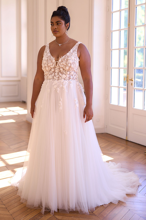 Eine Frau mit elegantem cremefarbenem Brautkleid und floralen Applikationen steht nachdenklich im Sonnenlicht