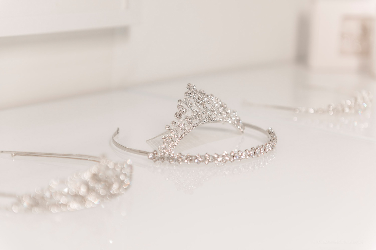 Eine funkelnde silberne Tiara mit glänzenden Steinen liegt auf weißem Untergrund