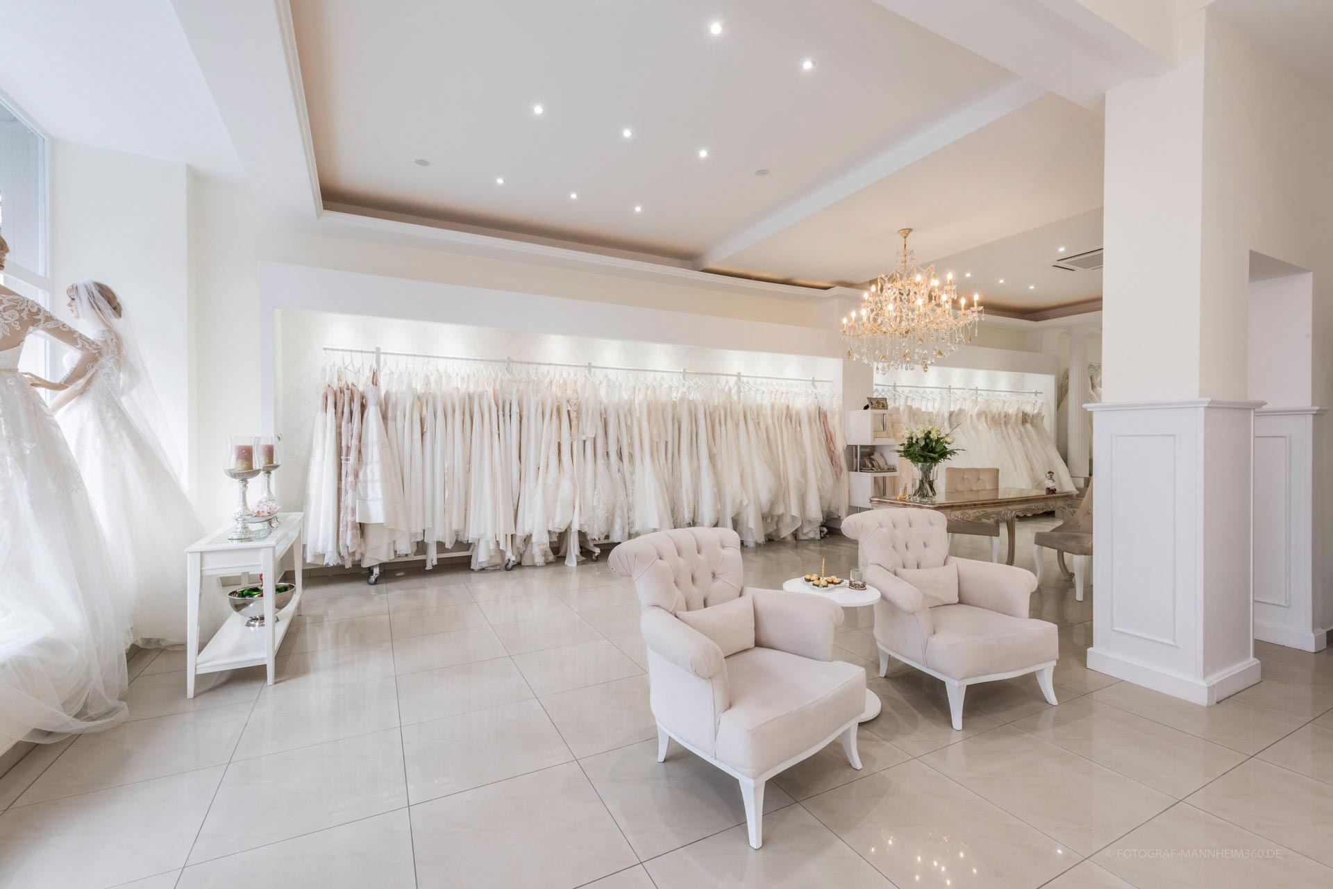 Ein eleganter Brautmodenladen mit weißen Kleidern, Kristalllüster und bequemen Sesseln