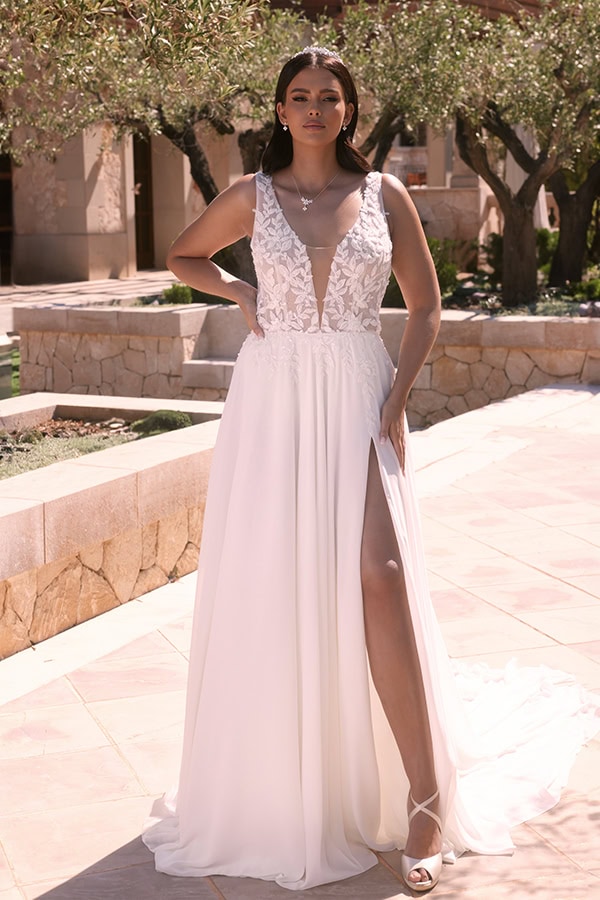 Eine Frau mit ernster Miene trägt ein weißes Kleid mit Spitzenoberteil und Beinschlitz