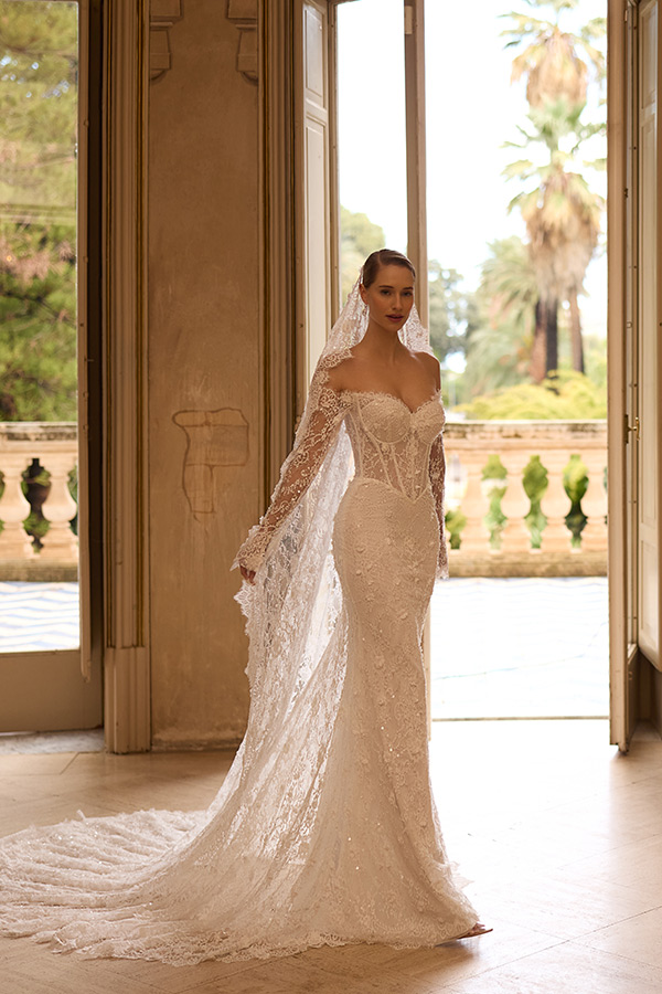 Eine elegant gekleidete Braut mit einem Spitzenkleid und Schleier steht vor offenen Türen