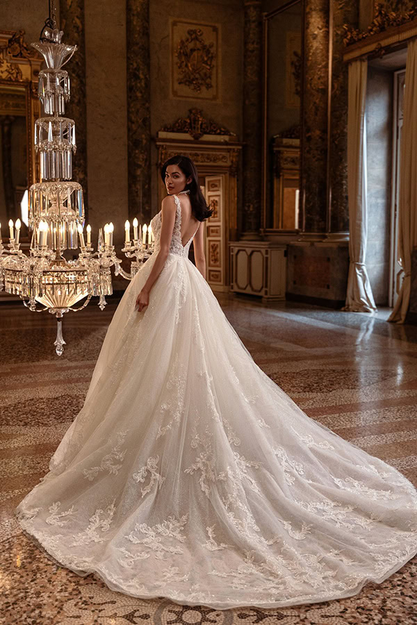 Eine elegant gekleidete Frau in weissem Brautkleid steht lächelnd in prunkvollem Saal