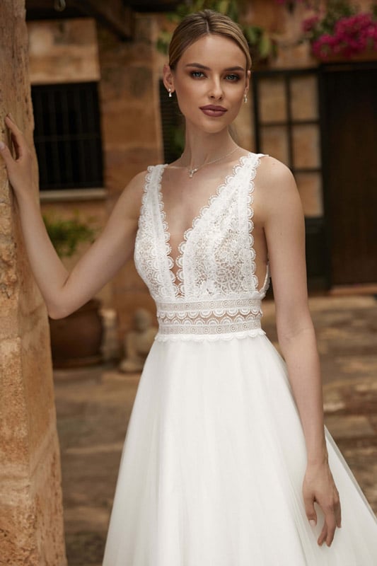 Junge Frau mit elegantem weißem Spitzenkleid und sanftem Lächeln in sonnigem Garten