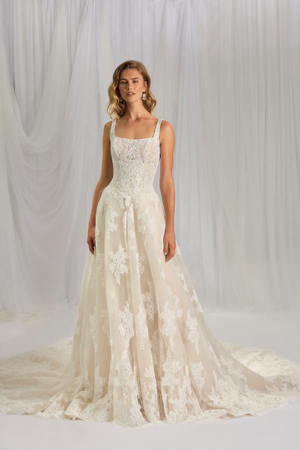 Eine Frau mit leichtem Lächeln trägt ein elegantes, cremefarbenes Spitzenkleid