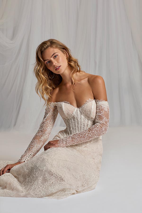 Eine blonde Frau im cremefarbenen Spitzenkleid sitzt entspannt mit leichtem Lächeln