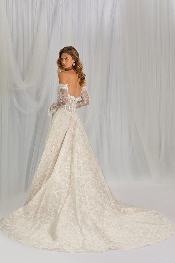 Eine Frau mit sanftem Lächeln trägt ein cremefarbenes Spitzenkleid mit Schleppe