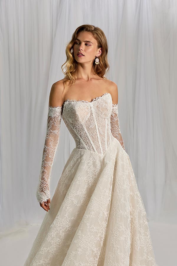 Eine junge Frau mit langen blonden Haaren trägt ein cremefarbenes Spitzenkleid und blickt entspannt zur Seite