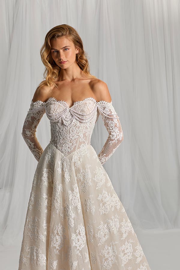 Eine blonde Frau mit ernstem Gesichtsausdruck trägt ein schulterfreies Spitzenkleid