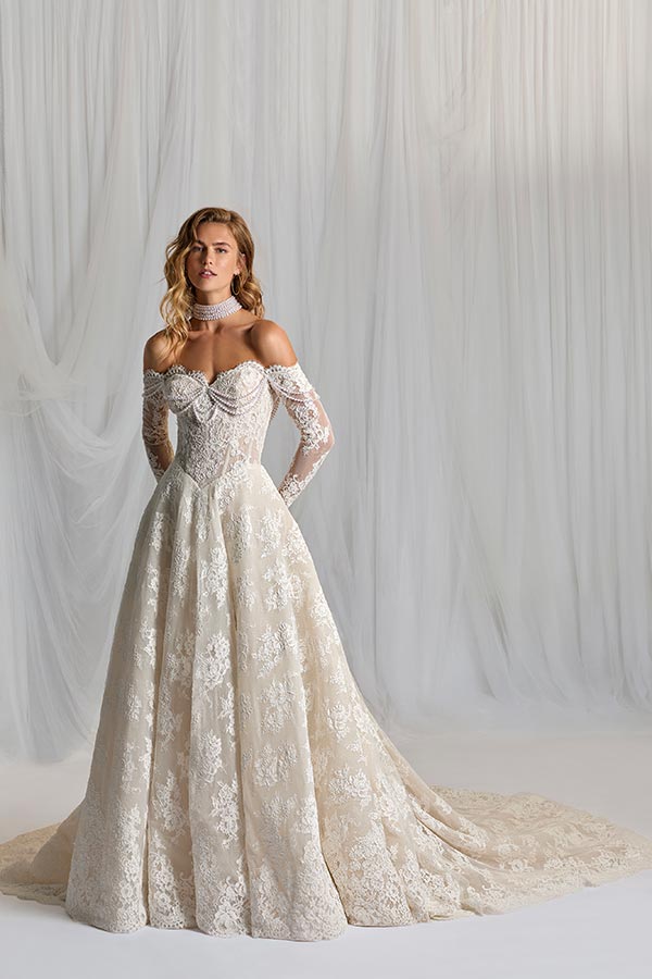 Blonde Frau mit entspanntem Blick trägt ein cremefarbenes Spitzenkleid mit Schleppe