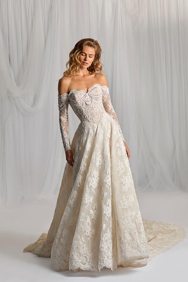 Eine blonde Frau mit ruhigem Blick trägt ein cremefarbenes, langes Spitzenkleid