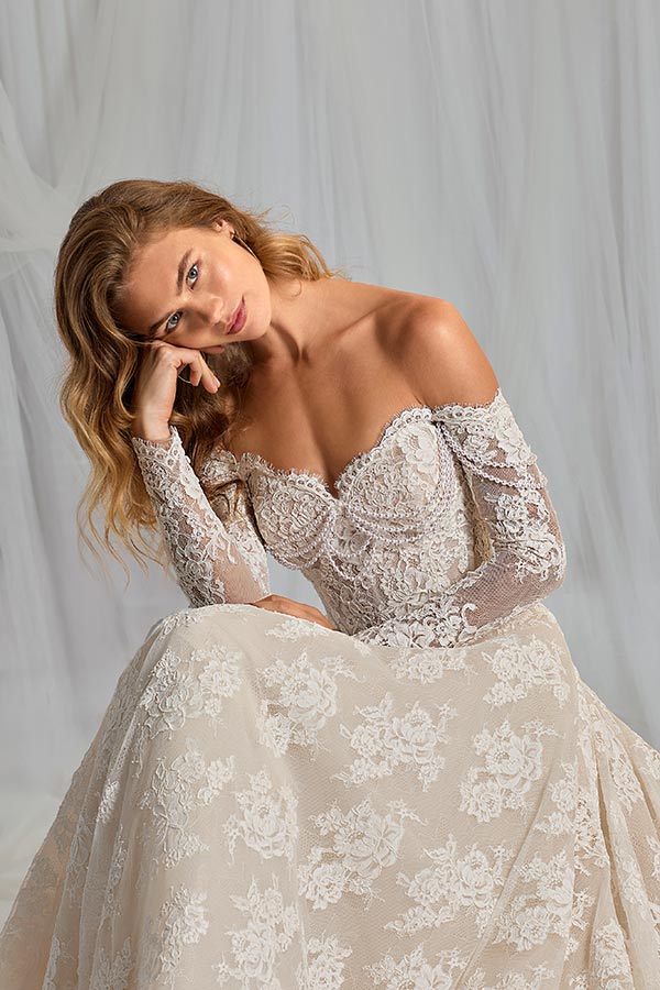 Junge Frau mit langen blonden Haaren lächelt nachdenklich im Spitzenbrautkleid