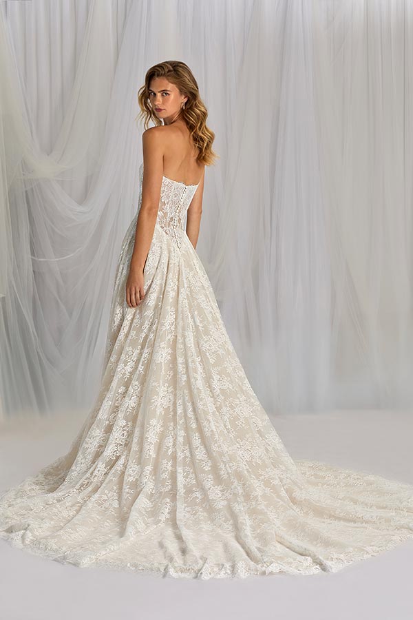 Eine junge Frau mit welligem blonden Haar trägt ein elegantes Spitzenkleid in Creme und blickt ruhig über die Schulter