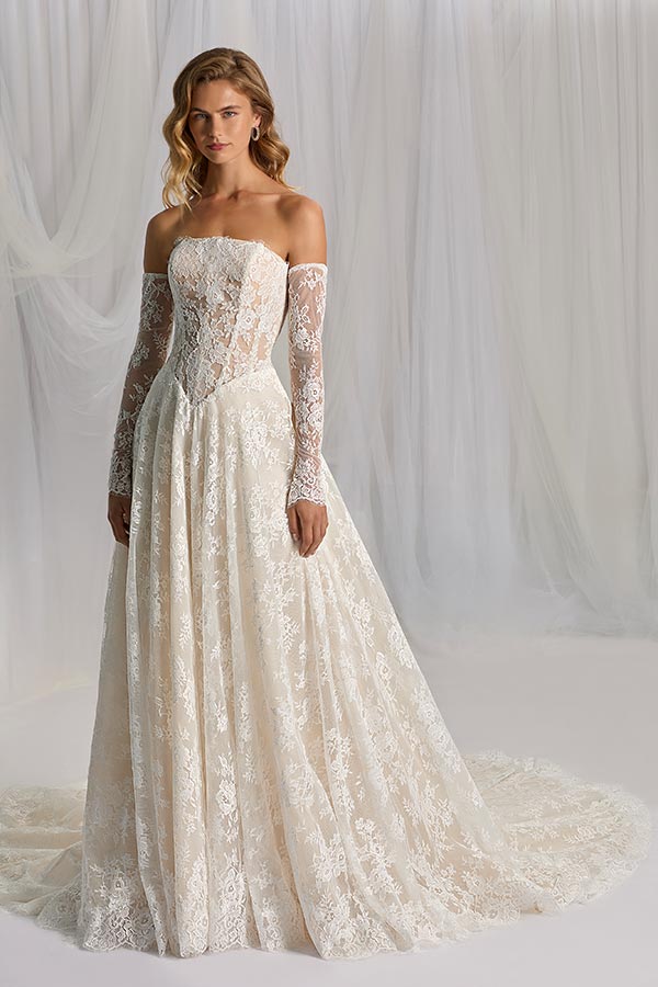 Eine junge Frau mit neutralem Gesichtsausdruck trägt ein cremefarbenes Spitzenkleid