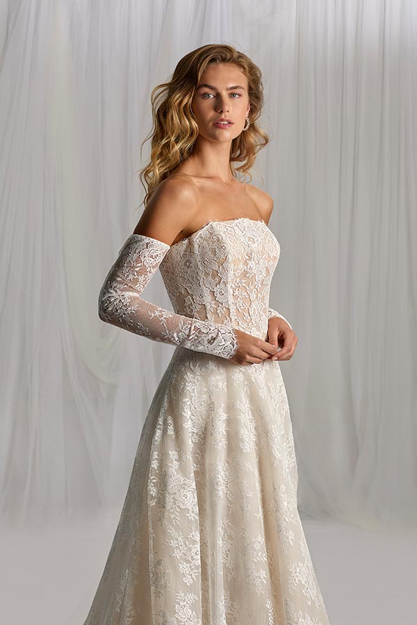 Junge Frau mit offenen blonden Haaren in cremefarbenem Spitzenkleid wirkt elegant