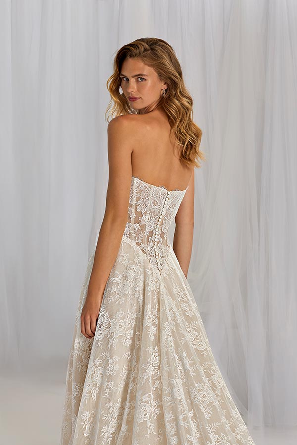 Eine junge Frau mit langen blonden Haaren trägt ein elegantes Spitzenkleid und blickt ernst