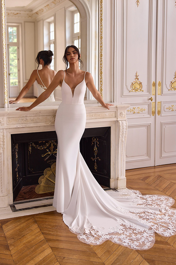 Eine Frau im eleganten weißen Brautkleid steht entspannt vor einem Kamin