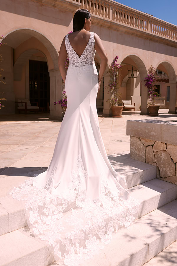 Eine Frau im eleganten weißen Brautkleid mit Spitzenrücken steht auf Steintreppen