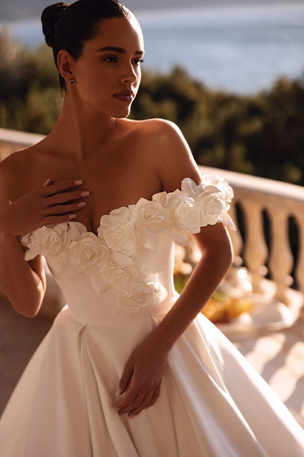 Eine Frau mit elegantem Gesichtsausdruck trägt ein weißes Brautkleid mit Blumendetails